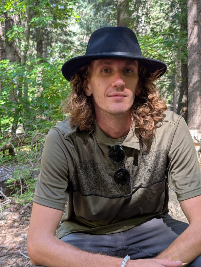 Tyler High in a wide-brimmed hat, sitting in a pine forest